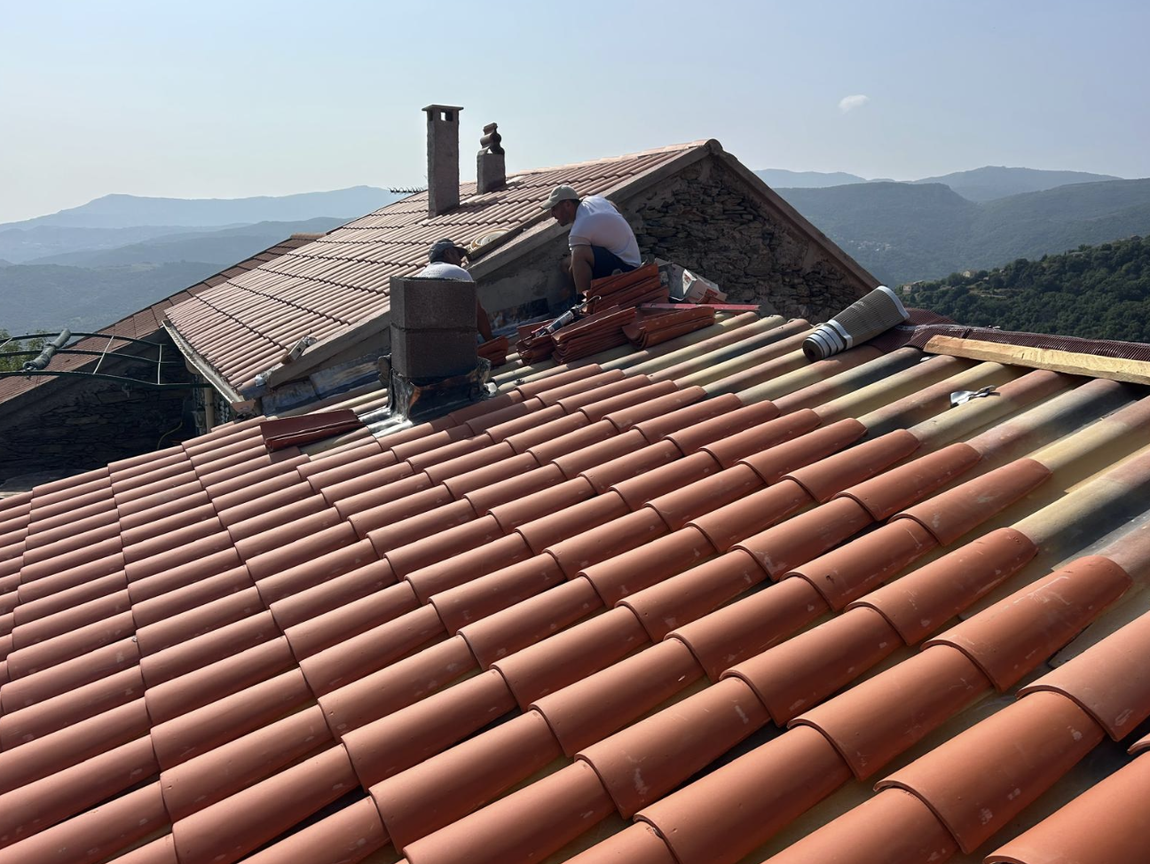 Couvreurs posant des tuiles sur un toit face aux montagnes corses