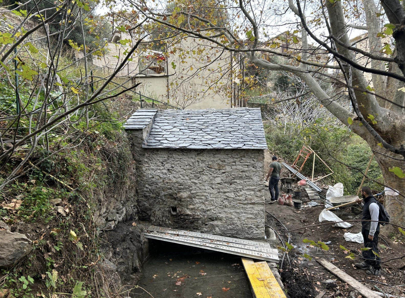 Petit bâtiment en pierre avec toiture en lauze neuve au bord d'un ruisseau